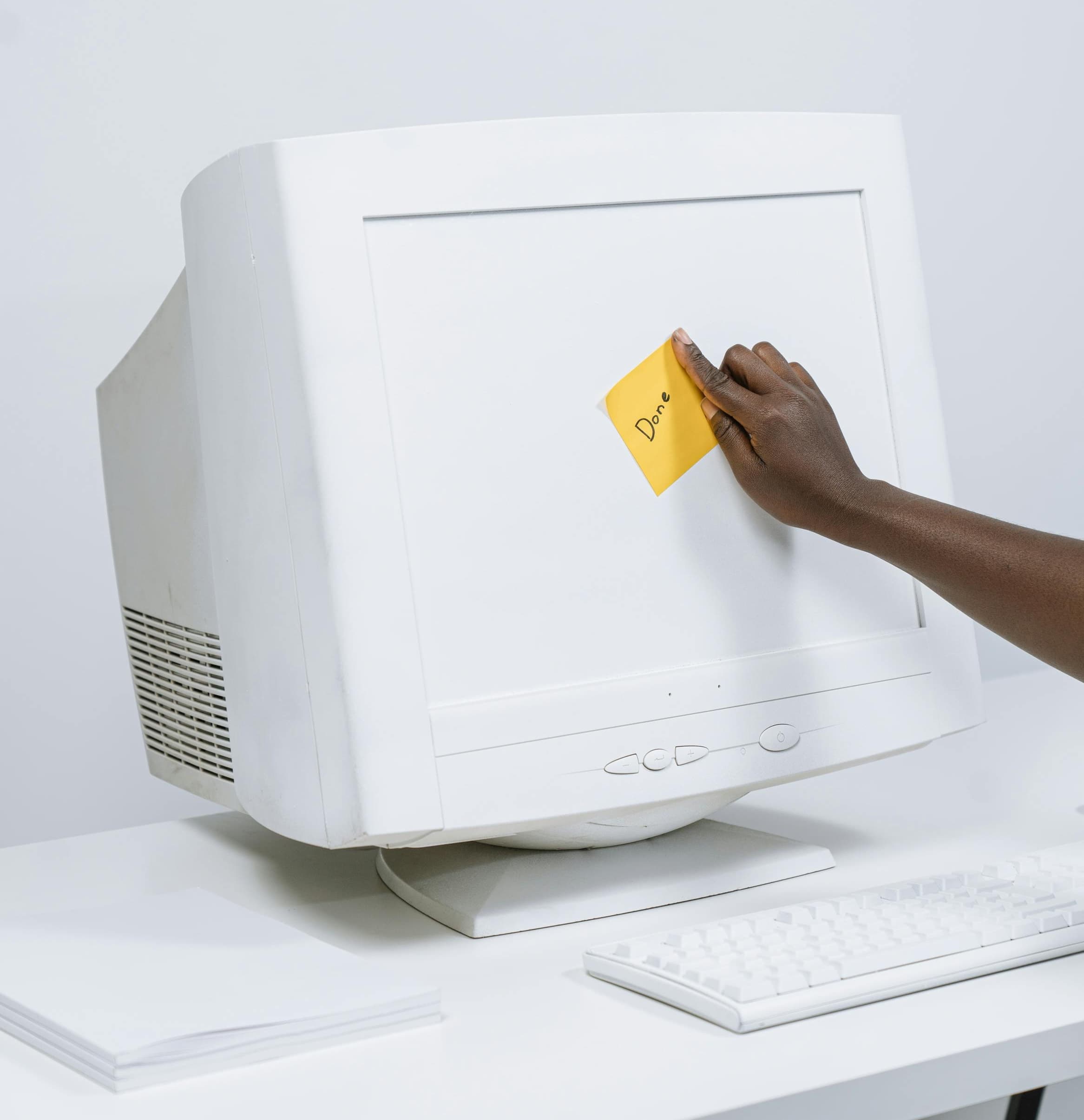 Hand placing a 'Done' sticky note on a CRT monitor